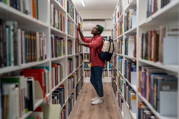 Thoughtful Black student guy searching materials for educational research in college library. Young...