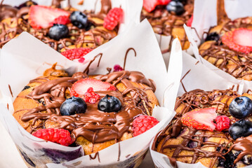 Several muffins on a plate, covered with chocolate icing, strawberries and blueberries