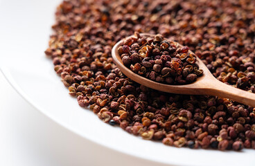 Sichuan pepper, wooden spoon and plate set against a white background.