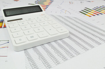 Wide angle image of white calculator on documents with charts and numbers.