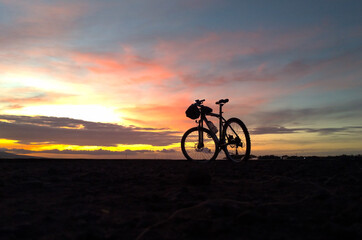 Naklejka na ściany i meble Silhouette of mountain bike by the beach with dramatic sunrise background.