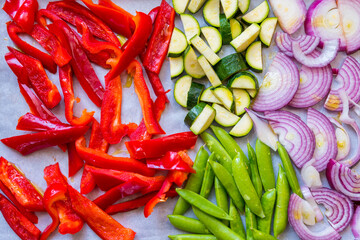 Sliced and chopped colorful fresh vegetables food preparation top view. Red peppers, pea pods, zucchini, and onions on baking sheet