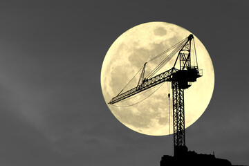 Silhouettes of construction cranes in the full moon atmosphere.