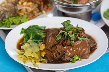 Stewed pork knuckle on a white plate with a side dish of vegetables and appetizers.