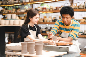 Young African American boy wearing apron preparing pots and sculptures using mud and and clay and painting them in a workshop studio while decorating them using brushes