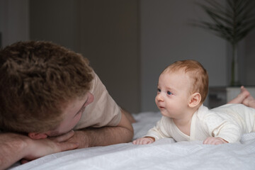 Cute two or three months baby boy looking at his parent or adult lying on belly on bed.Copy space.