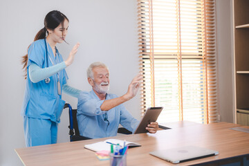 Smiling and cheerful senior male patient using digital tablet for video call with nurse in uniform and stethoscope standing waving hand at screen in a medical room in hospital