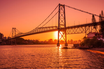 Fototapeta na wymiar Hercilio luz bridge with warm sunset and reflection on water in Florianopolis