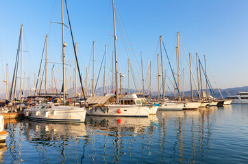 Fototapeta na wymiar Greece. Crete Island. Beautiful seascape with yachts in Agios Nikolaos Marina in sunset. The masts of yachts are reflected in the blue water of the Mirabello Bay. Summer travel and seaside holidays
