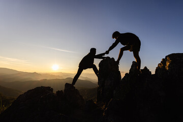 Silhouette Teamwork, Male hikers climbing up mountain cliff and one of them giving helping hand....