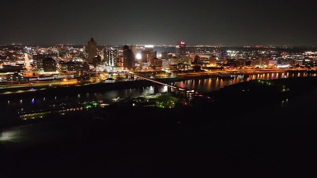 Memphis, Tennessee skyline with Mississippi River pulling back to Hernado De Soto bridge with drone video at night.