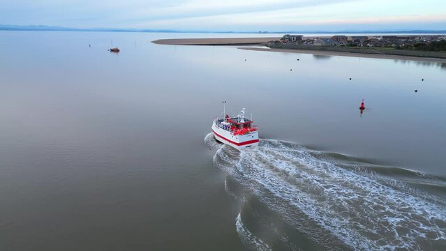 Fishing trawler heading out to sea on calm water at dusk on River Wyre Estuary Fleetwood Lancashire UK with Knott End