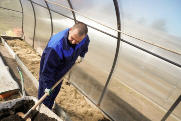 A man works in a vegetable garden in early spring.  Digs the ground.   Working in a greenhouse