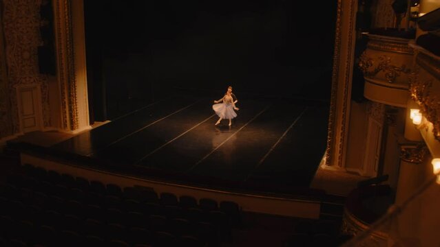 Establishing shot of ballet dancers practicing choreography on classic theater stage. Man and woman prepare theatrical dance performance. Classical ballet dance. Rows of chairs. Dramatic lighting.
