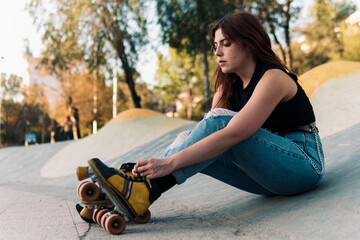 mujer joven adolescente descansando y acomodando sus patines en un parque con luz natural.