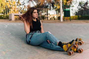 mujer adolescente descansando y peinando su cabello en un parque con sus patines al atardecer.