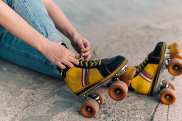 vista desde cerca de patines de cuatro ruedas de colores, con manos de mujer acomodando cordones.
