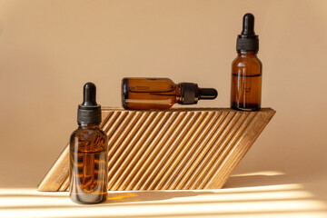 Bottles with cosmetic serum on wooden platform. Glass vials with a dropper lid in sunlight. Amber...