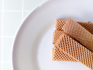Obraz na płótnie Canvas Chocolate wafers on a white plate with copy space. Sweet wafers on a plate with negative space. Top view of chocolate thin crisp biscuit. Brown small flat sweet cakes.