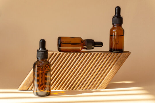 Bottles with cosmetic serum on wooden platform. Glass vials with a dropper lid in sunlight. Amber cosmetic packaging on a brown background. Conceptual mockup, branding