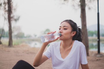 An Asian woman is drinking a water after exercising, running, jogging or morning work out. Concept of sport advertising, Bottle of mineral water, refreshing and relaxing, resting after running. Energy