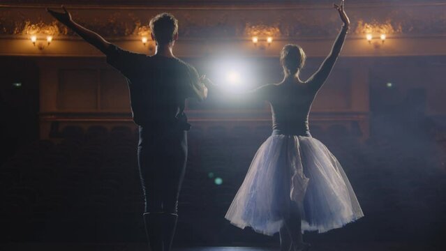 Ballet dancers bowing during choreography rehearsal on classic theater stage illuminated by spotlight. Man and woman prepare theatrical dance performance. Art of classical ballet dance. Slow motion.