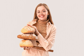 Young woman with loaves of fresh bread on light background