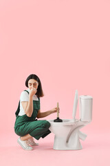 Fototapeta na wymiar Female plumber with plunger and toilet bowl on pink background
