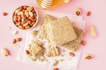 Tasty halva and bowl of peanuts on pink background