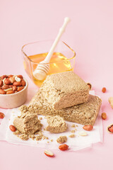 Tasty halva, peanuts and honey on pink background