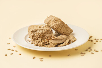 Plate of tasty halva with sunflower seeds on yellow background
