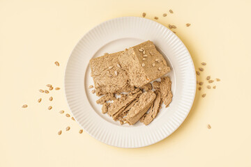 Plate of tasty halva with sunflower seeds on yellow background
