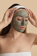 Young woman with applied clay mask on beige background, closeup