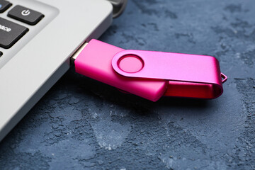 Modern laptop with pink USB flash drive on blue grunge background