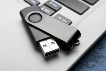 Black USB flash drive on modern laptop, closeup