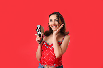 Obraz premium Young pin-up woman with retro video camera on red background
