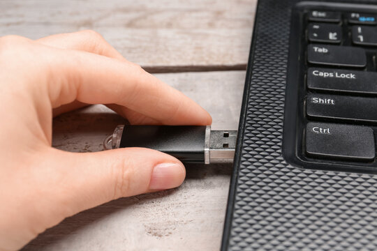Woman using black USB flash drive with modern laptop on white wooden background