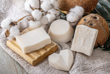 Cute pieces of white natural soap, soap dish, coconut and cotton on the table