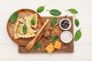 Board with pieces of delicious quiche, cheese and spices on white wooden background