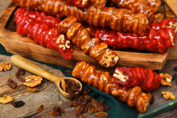 Board with delicious churchkhela and spoon of raisins on wooden table, closeup