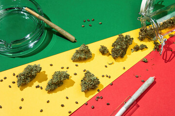 On a rasta background lie dry buds of medical marijuana from a glass jar, mixed with seeds, and...