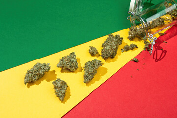 On a rasta background lie dry buds of medical marijuana pouring out of a glass jar