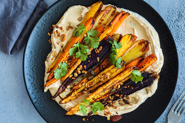 Multicolored baked carrots with hummus on black plate. Vegan recipe.