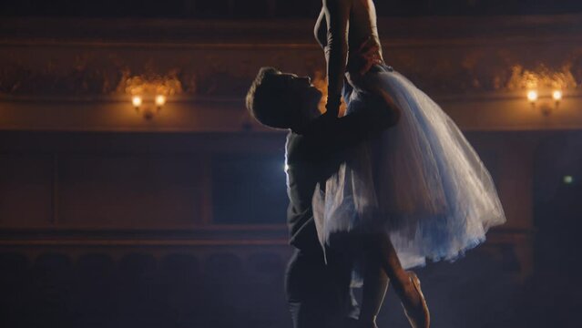 Ballet dancers practice and rehearse choreography on classic theater stage illuminated by spotlight. Man and woman prepare for theatrical dance performance. Art of classical ballet dance. Slow motion.