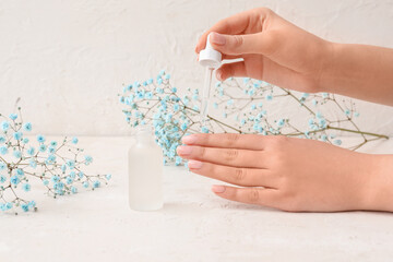 Female hands with bottle of cuticle oil and gypsophila flowers on light background