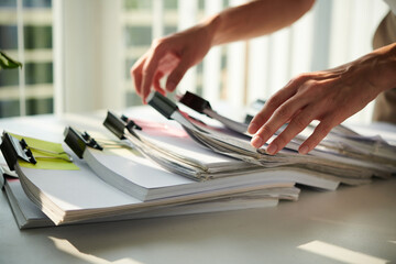 Closeup image of female entrepreneur taking documents from stack on office table