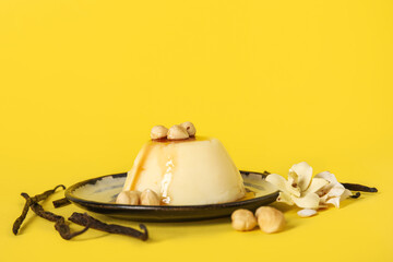 Plate with delicious pudding, hazelnuts and vanilla sticks covered by caramel syrup on yellow background