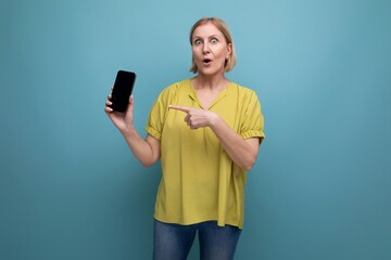 Naklejka premium surprised blond middle-aged woman holding a gadget phone in her hands vertically with a mockup