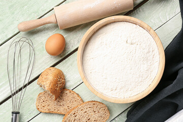 Bowl with wheat flour, bread, egg and utensils on green wooden table