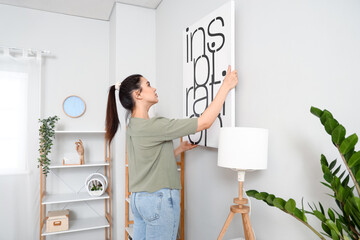 Young woman hanging picture on wall in living room